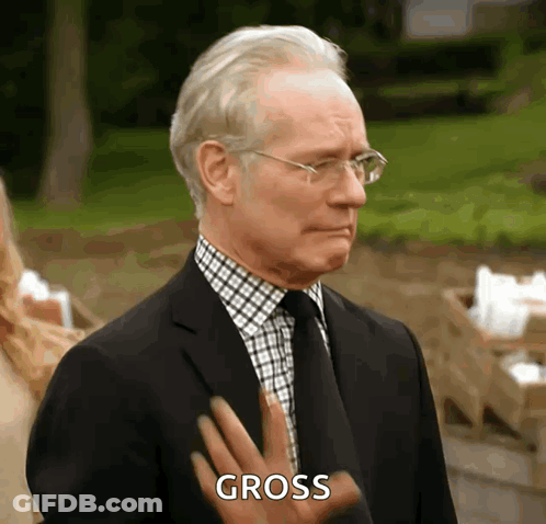 A Man In A Suit And Tie Is Making A Gross Gesture With His Hand GIF