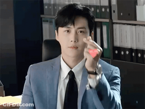 A Man In A Suit And Tie Is Making A Heart Shape With His Hands . GIF