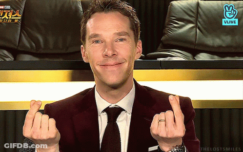 A Man In A Suit And Tie Is Making A Heart With His Hands GIF