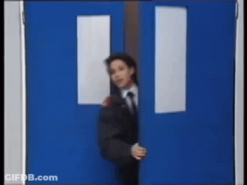 A Man In A Suit And Tie Is Peeking Out From Behind A Blue Door GIF
