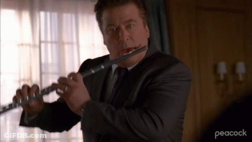 A Man In A Suit And Tie Is Playing A Flute With Peacock Written On The Bottom GIF