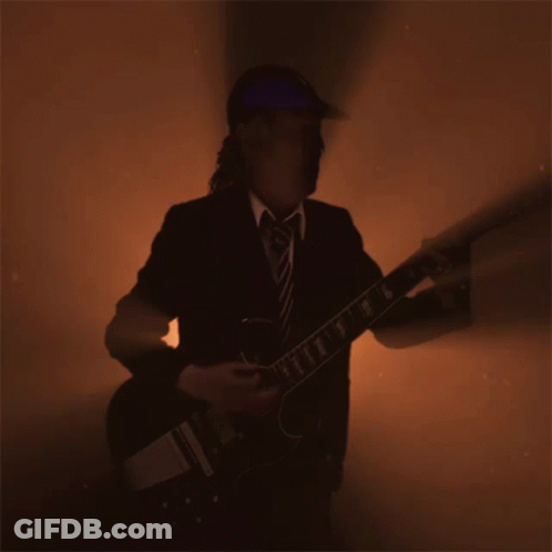 A Man In A Suit And Tie Is Playing A Guitar In A Dark Room GIF