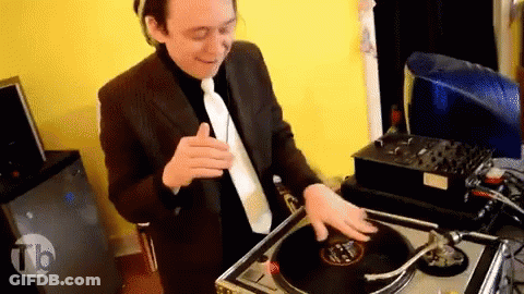 A Man In A Suit And Tie Is Playing A Record On A Turntable With The Letters Tb On The Bottom Right GIF