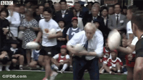 A Man In A Suit And Tie Is Playing Rugby In Front Of A Crowd Of People . GIF