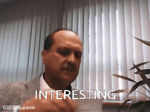 A Man In A Suit And Tie Is Pointing At Something Interesting GIF
