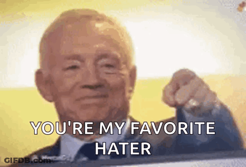 A Man In A Suit And Tie Is Pointing At The Camera . GIF