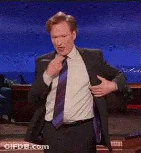 A Man In A Suit And Tie Is Pointing At The Camera . GIF