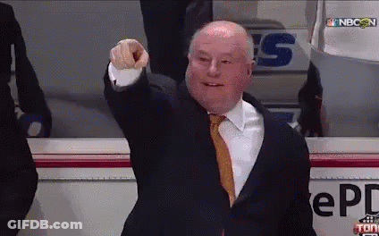 A Man In A Suit And Tie Is Pointing At The Camera In Front Of A Sign That Says Nbc On It GIF