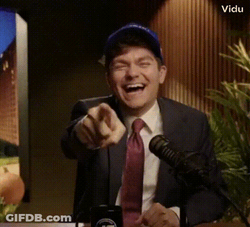 A Man In A Suit And Tie Is Pointing At The Camera While Laughing GIF