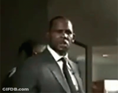 A Man In A Suit And Tie Is Pointing At The Camera . GIF