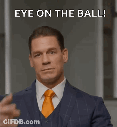 A Man In A Suit And Tie Is Pointing His Finger At His Eye With The Words Eye On The Ball Below Him GIF