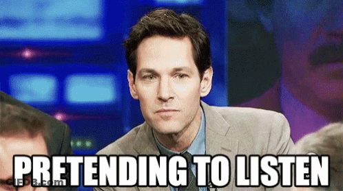 A Man In A Suit And Tie Is Pretending To Listen While Sitting In Front Of A Crowd . GIF