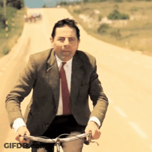 A Man In A Suit And Tie Is Riding A Bike On A Dirt Road GIF