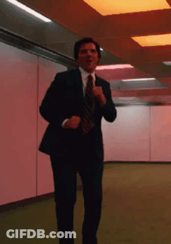 A Man In A Suit And Tie Is Running In A Hallway GIF