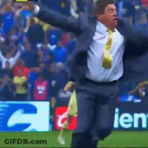 A Man In A Suit And Tie Is Running On A Field In Front Of A Sign That Says Ien GIF