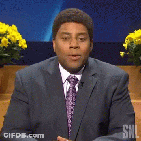 A Man In A Suit And Tie Is Saying Boo While Sitting On A Stage . GIF
