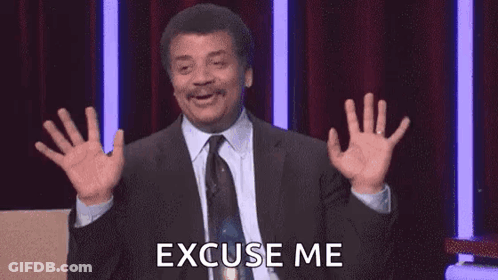 A Man In A Suit And Tie Is Saying Excuse Me With His Hands In The Air . GIF