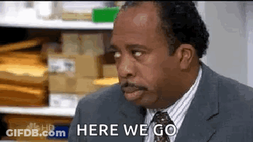 A Man In A Suit And Tie Is Saying `` Here We Go '' While Looking At Something . GIF