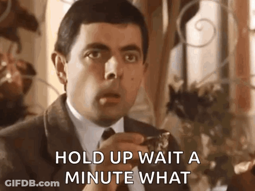 A Man In A Suit And Tie Is Saying `` Hold Up Wait A Minute What '' While Eating A Piece Of Food . GIF