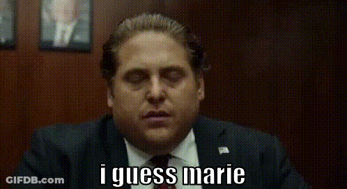 A Man In A Suit And Tie Is Saying I Guess Marie While Sitting In A Chair . GIF