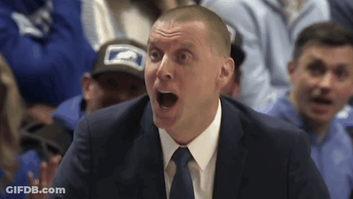 A Man In A Suit And Tie Is Screaming In Front Of A Crowd GIF