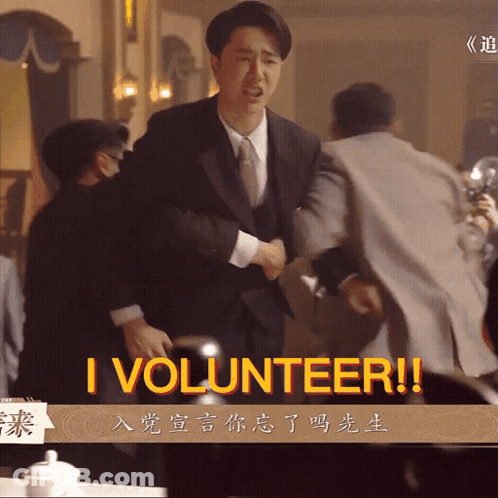 A Man In A Suit And Tie Is Shaking Hands With Another Man And The Words I Volunteer Are On The Screen GIF