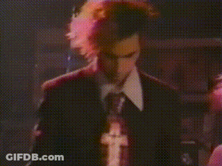 A Man In A Suit And Tie Is Singing Into A Microphone In A Dark Room GIF