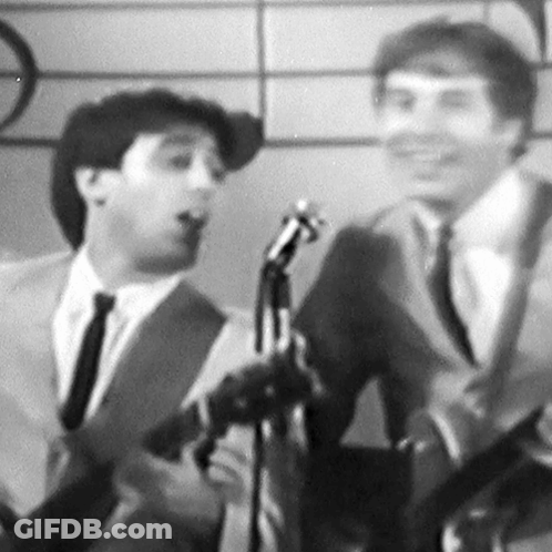 A Man In A Suit And Tie Is Singing Into A Microphone GIF