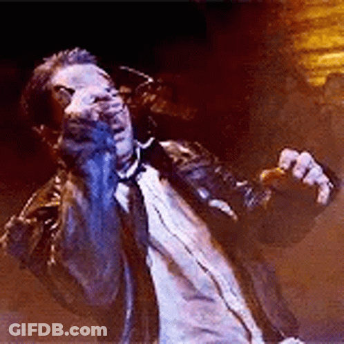 A Man In A Suit And Tie Is Singing Into A Microphone While Standing On A Stage . GIF