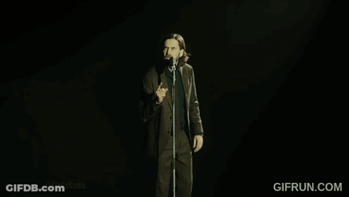 A Man In A Suit And Tie Is Singing Into A Microphone With Gifrun.com In The Corner GIF