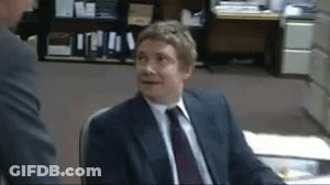 A Man In A Suit And Tie Is Sitting At A Desk GIF