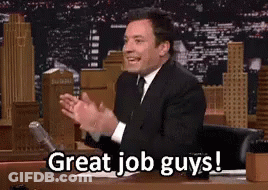 A Man In A Suit And Tie Is Sitting At A Desk And Applauding . GIF