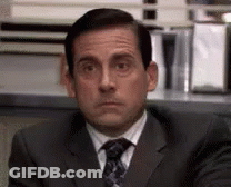 A Man In A Suit And Tie Is Sitting At A Desk And Looking At The Camera . GIF