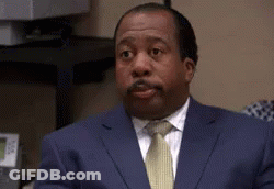 A Man In A Suit And Tie Is Sitting At A Desk And Making A Funny Face . GIF