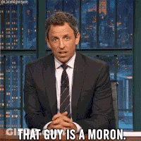 A Man In A Suit And Tie Is Sitting At A Desk And Says That Guy Is A Moron GIF