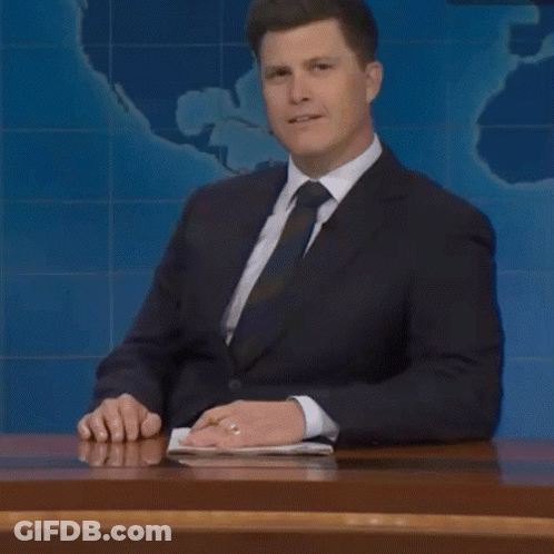 A Man In A Suit And Tie Is Sitting At A Desk And Talking About Something GIF