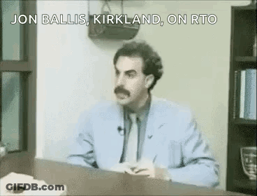 A Man In A Suit And Tie Is Sitting At A Desk And Talking . GIF