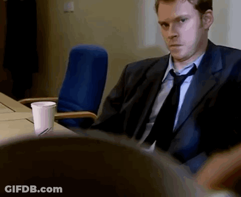 A Man In A Suit And Tie Is Sitting At A Desk . GIF