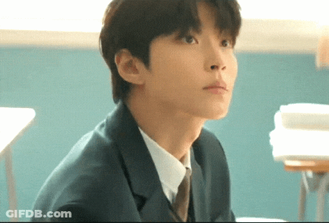 A Man In A Suit And Tie Is Sitting At A Desk In A Classroom . GIF