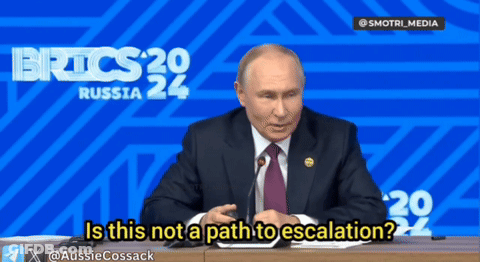 A Man In A Suit And Tie Is Sitting At A Desk In Front Of A Blue Background That Says Russia 24 GIF