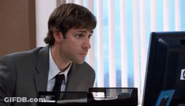 A Man In A Suit And Tie Is Sitting At A Desk In Front Of A Computer . GIF