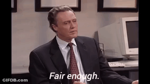 A Man In A Suit And Tie Is Sitting At A Desk In Front Of A Computer . GIF