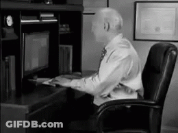 A Man In A Suit And Tie Is Sitting At A Desk In Front Of A Computer Monitor . GIF