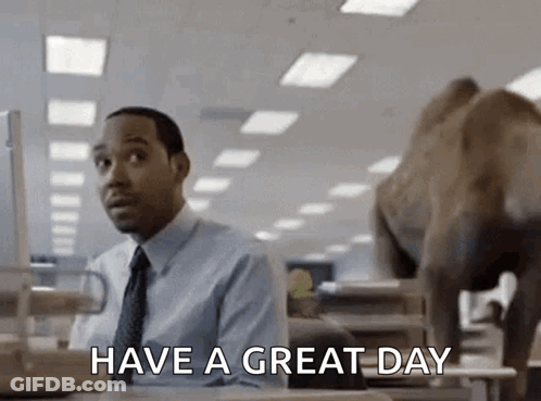A Man In A Suit And Tie Is Sitting At A Desk In Front Of A Computer While A Camel Walks Behind Him . GIF