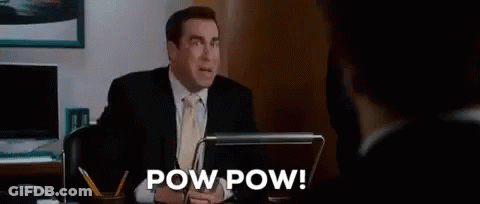 A Man In A Suit And Tie Is Sitting At A Desk In Front Of A Laptop Computer And Talking To Another Man . GIF