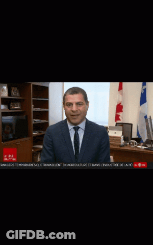 A Man In A Suit And Tie Is Sitting At A Desk In Front Of A Laptop Computer GIF