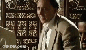 A Man In A Suit And Tie Is Sitting At A Desk In Front Of A Screen . GIF