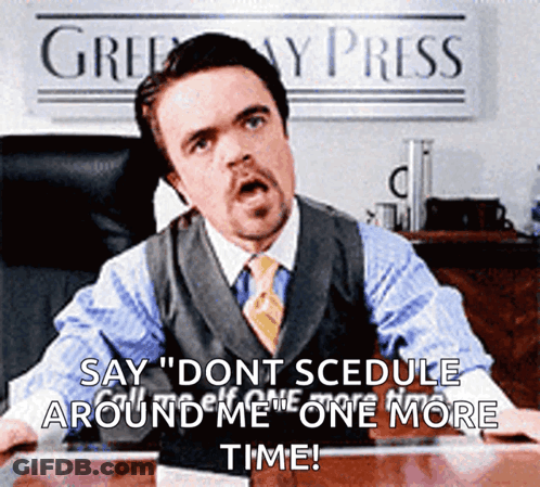 A Man In A Suit And Tie Is Sitting At A Desk In Front Of A Sign That Says ' Greenway Press ' GIF