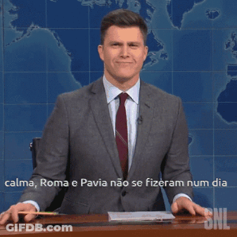 A Man In A Suit And Tie Is Sitting At A Desk In Front Of A Snl Sign GIF