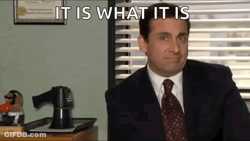 A Man In A Suit And Tie Is Sitting At A Desk In Front Of A Window In An Office . GIF